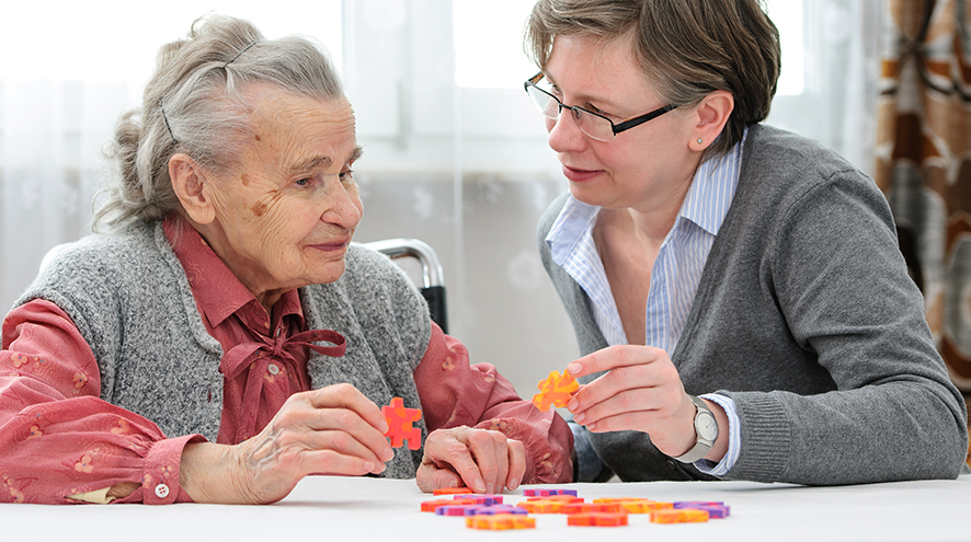 Middle-aged woman helping a senior woman complete a puzzle.