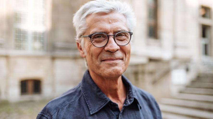 Senior man with glasses and wearing a blue shirt, smiling.