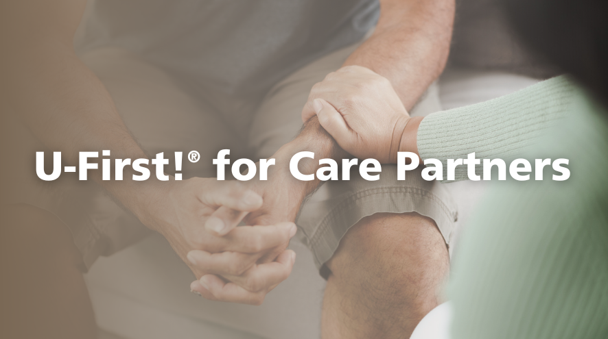 Close-up image of a person reaching out their hand to comfort another person with their hands clasped. The overset text reads "U-First for care partners."