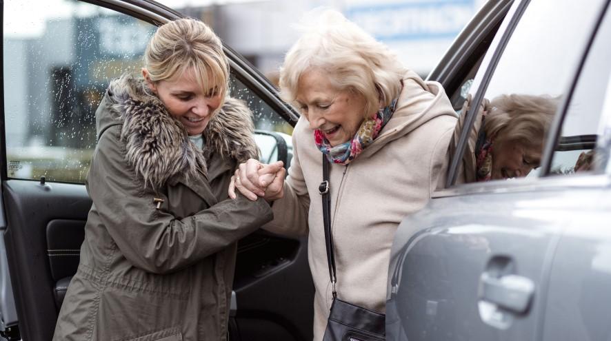 Middle-aged woman helping senior woman out of her car.