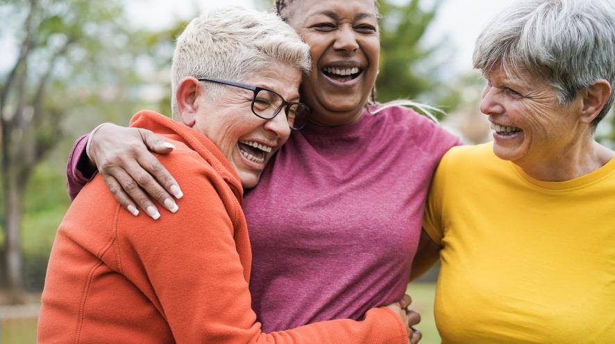 Three smiling older women embracing outdoors.