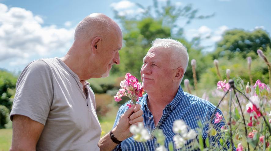An elderly couple, two light-skinned men, enjoying the flowers outdoors.