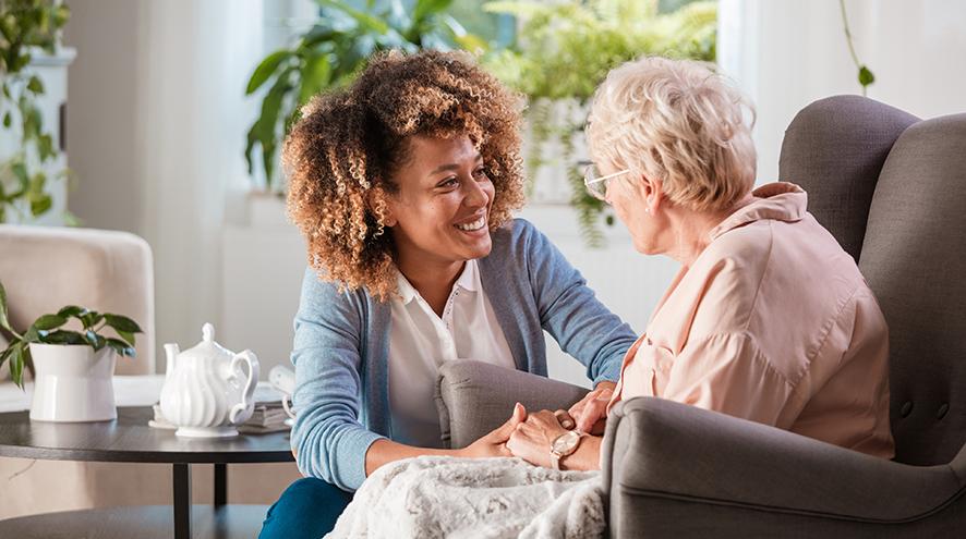 Professional caregiver having a conversation with a senior woman living with dementia at her home.