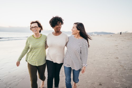 Three middle-aged women taking a walk on a beach together, looking happy and content.