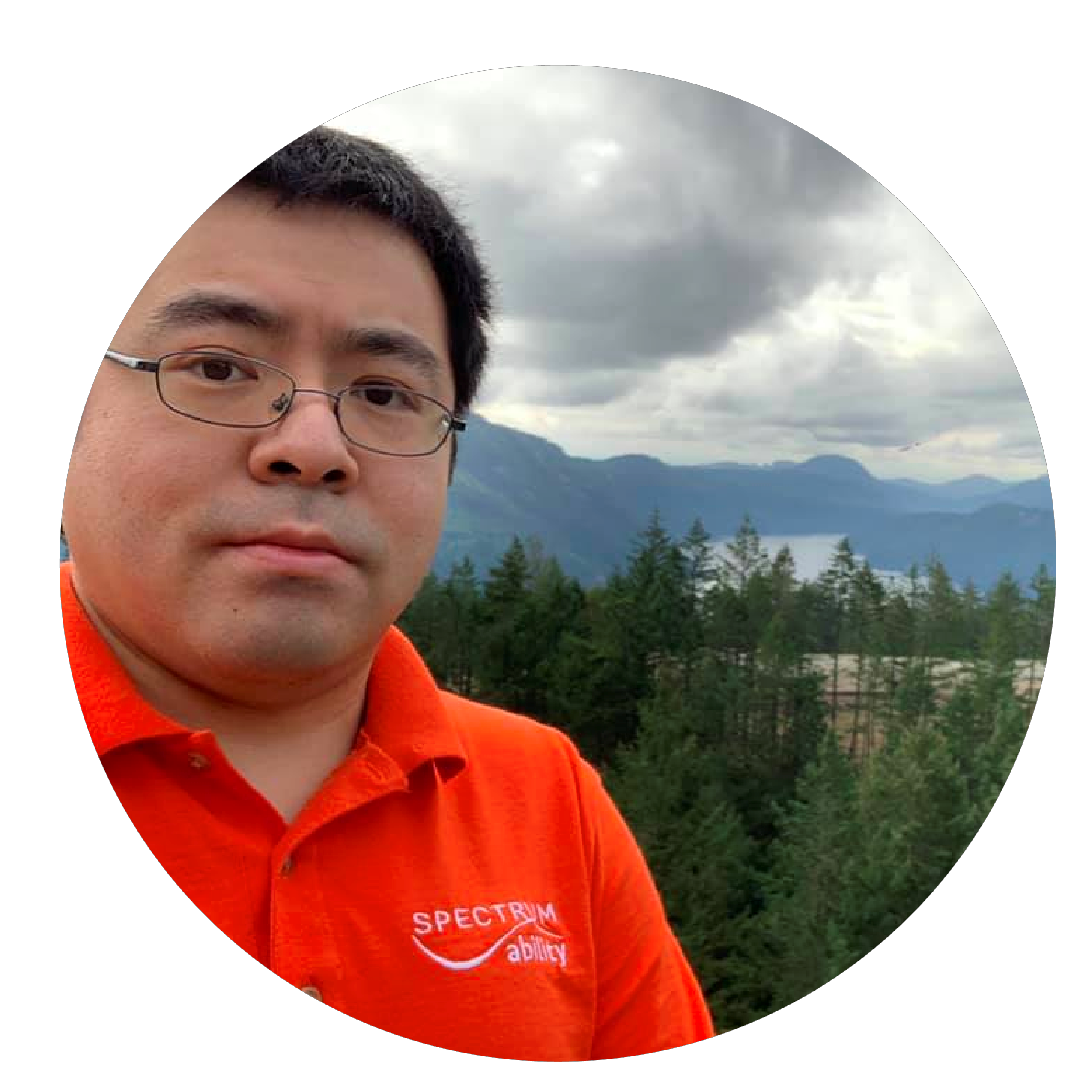 A man in glasses and a bright orange polo shirt with trees and mountains in background