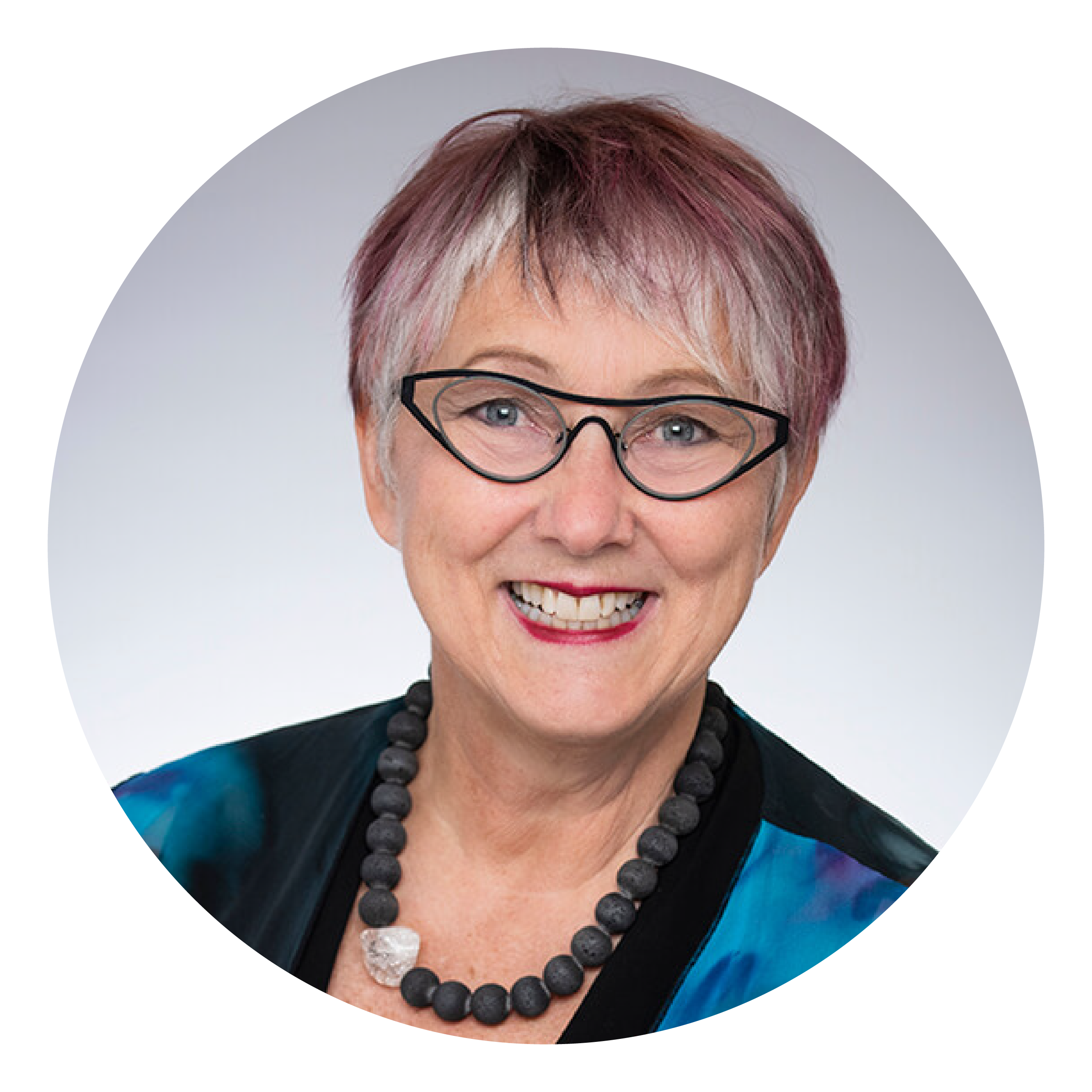 A smiling woman with short grey and purple hair and black glasses