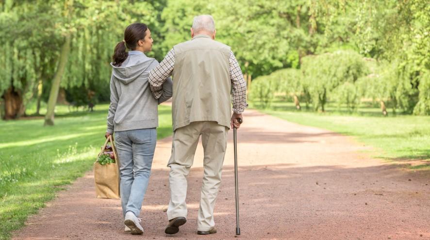 Caregiver and senior man living with dementia walking home together from the grocery store.