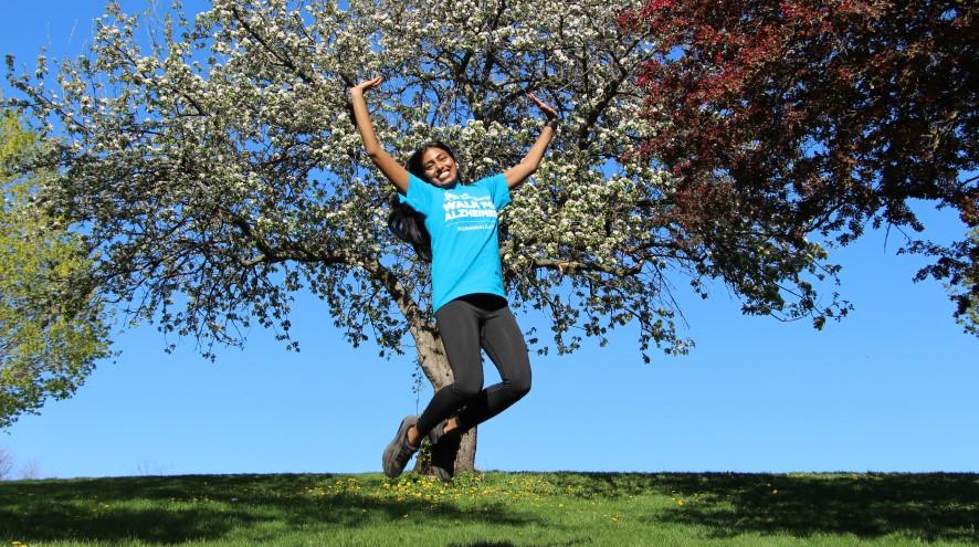 Young woman wearing a IG Wealth Management Walk for Alzheimer's shirt and jumping in joy in a park.