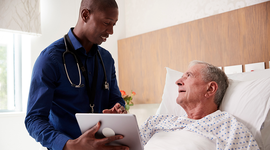 A doctor shows an older adult hospital patient something on a tablet.