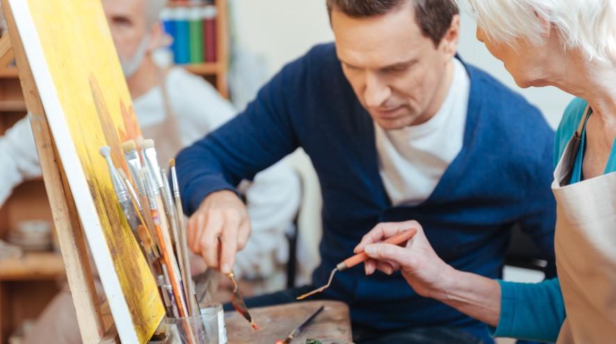 Two individuals, a middle-aged man and a senior woman, taking a painting class together.