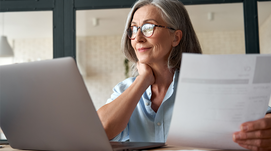 Older woman wearing glasses with laptop and papers.
