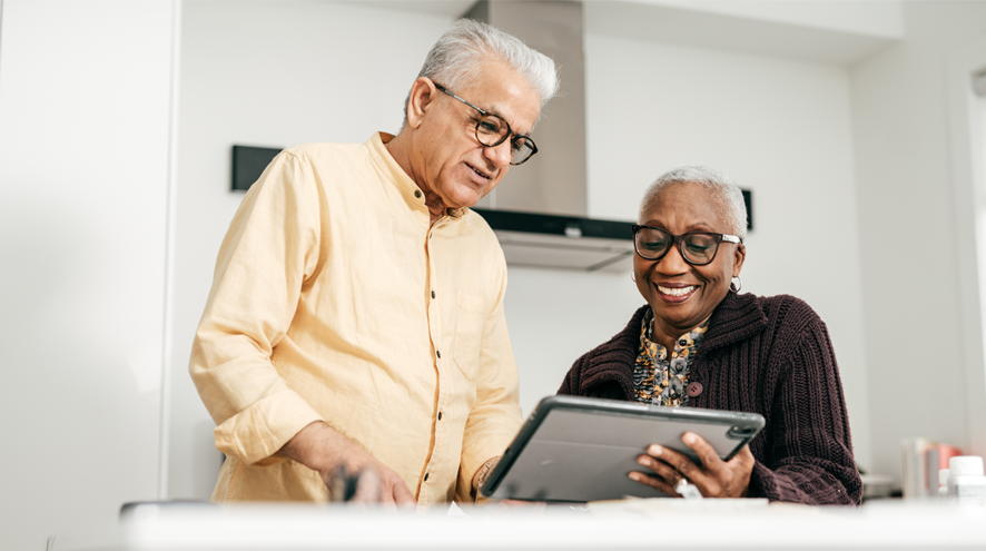 Older man and older woman look at tablet in kitchen