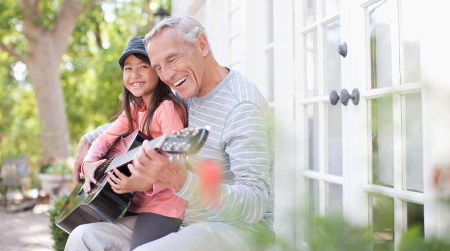 Older man playing guitar with small child on lap
