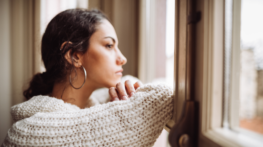A young adult woman looks out a window