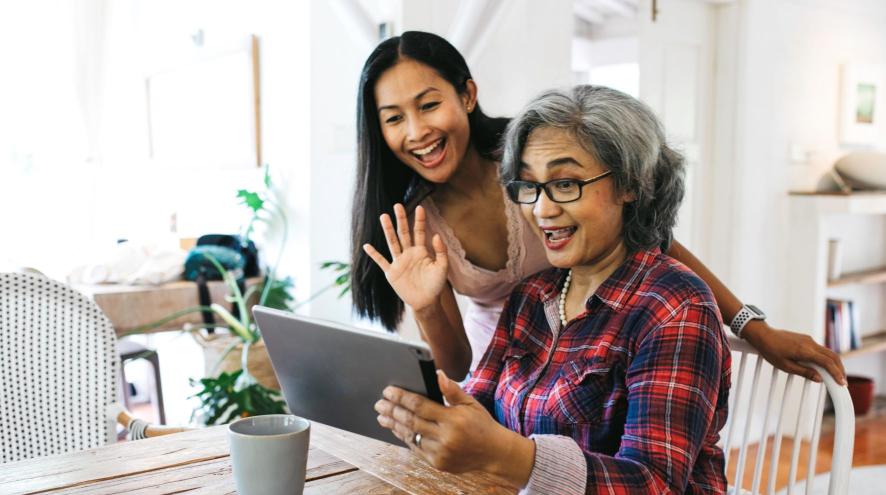 An older woman and a younger woman smile and wave during a video call