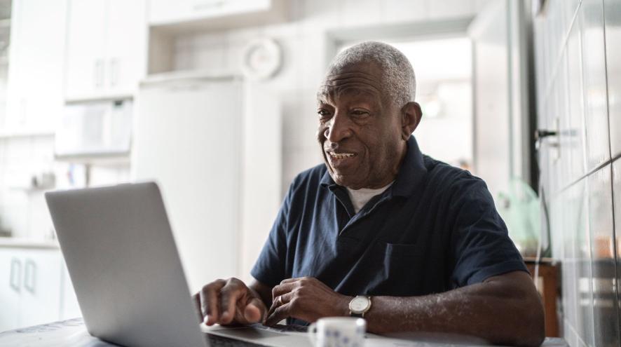 Older man sits with laptop at kitchen table