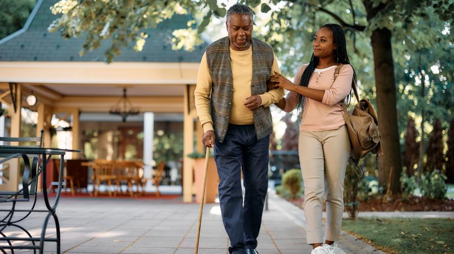 Older man walking with cane while a younger woman holds his arm