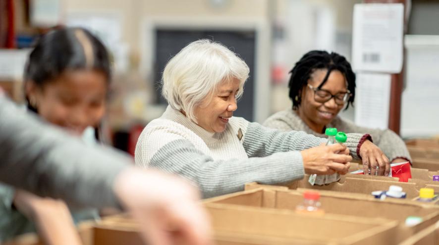 Three women of varying ages filling food bank boxes and shelves