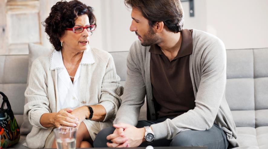 An older adult woman has a serious conversation with her adult son at home.