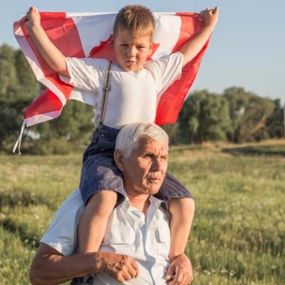 Young boy holding a Canadian flag and sitting on his grandfather's shoulders.