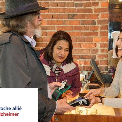 Two senior citizens having a pleasant conversation with a retail worker. The Proche allié Alzheimer logo is visible in the lower left corner.