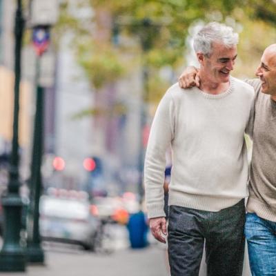 Two middle-aged men smiling happily and walking together down the street.