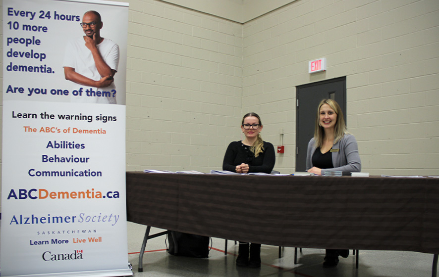Alzheimer Society Staff sitting at a booth with resources and a banner that says, "Every 24 hours, 10 more people develop dementia."