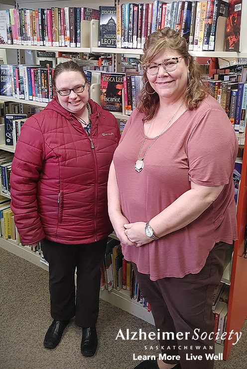 Our Dementia Community Coordinator standing in front of multiple book shelves with Saltcoats' Head Librarian