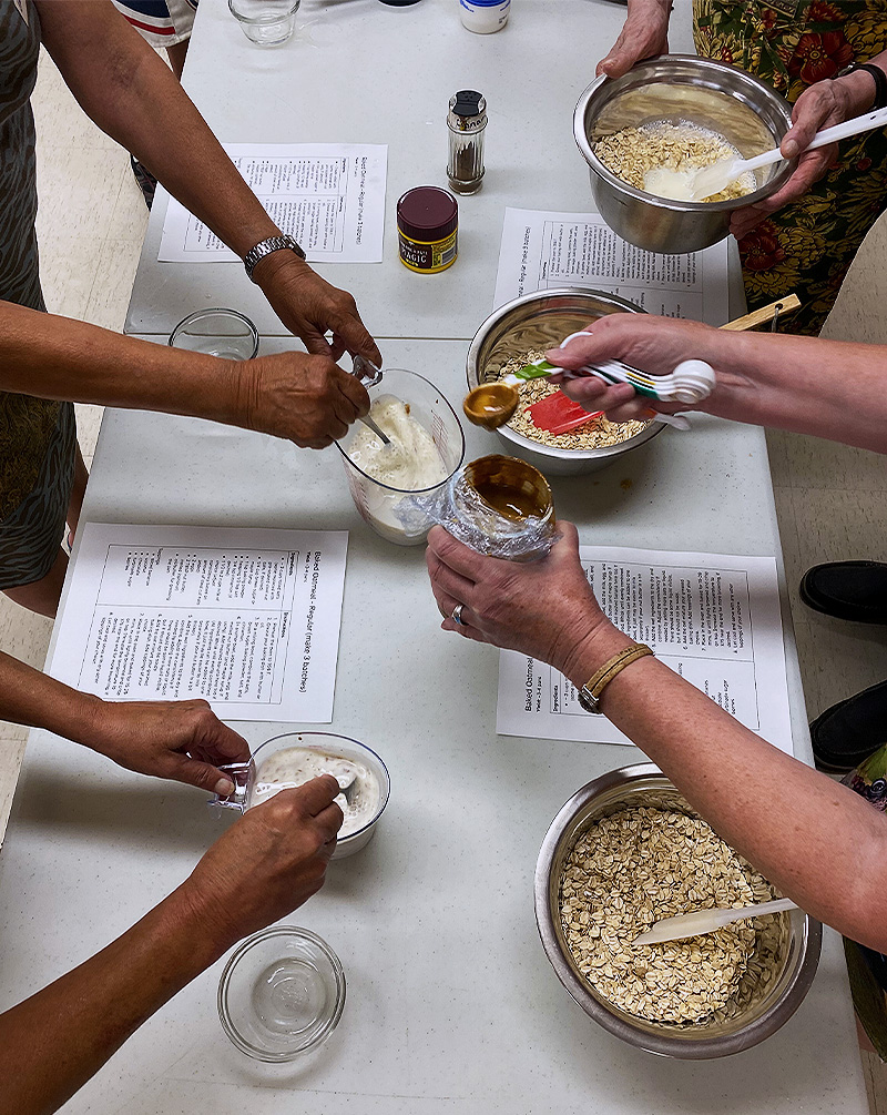 Four sets of hands working together to add and mix ingredients for baked oatmeal.