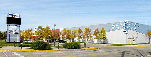 The Gallagher Centre parking lot sign. It is in front of a large parking lot with trees, and a large community complex.