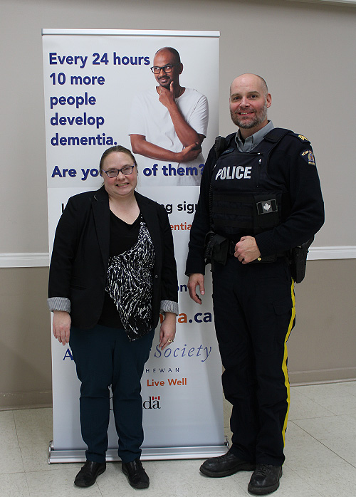 Our Dementia Community Coordinator standing next to a police officer in uniform in front of an Alzheimer Society sign that says, "Every 24 hours 10 more people develop dementia."