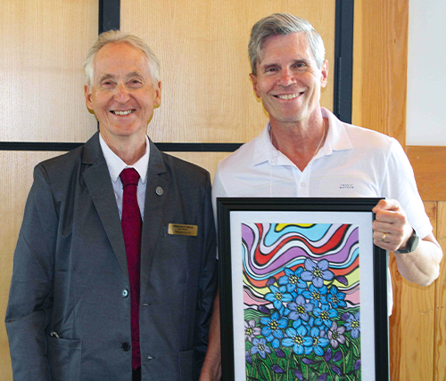 Two men standing next to each other smiling. The one on the right is holding a colourful Alzheimer Society of Saskatchewan framed award.