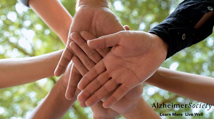 A stack of hands together in an outdoor team huddle.