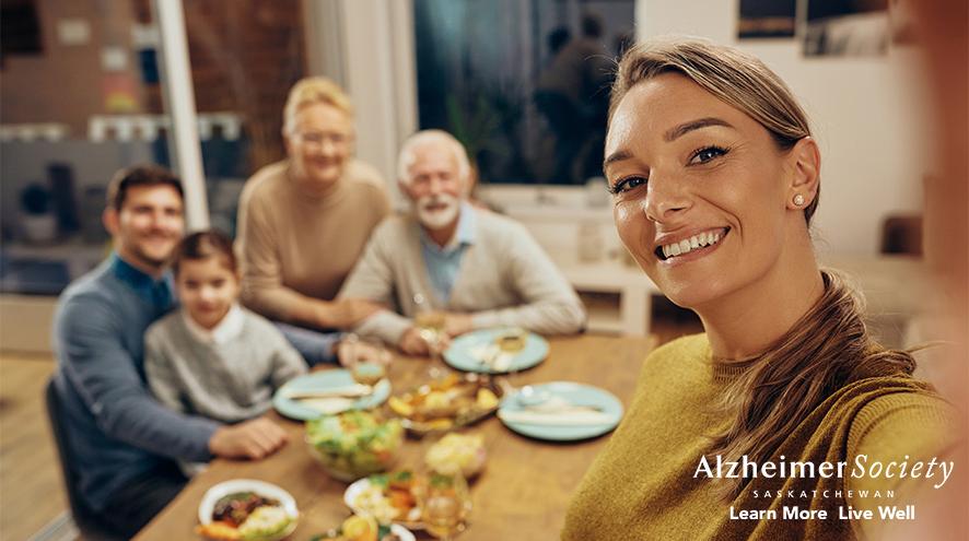 A woman taking a selfie in front of her extended family at the dinner table.