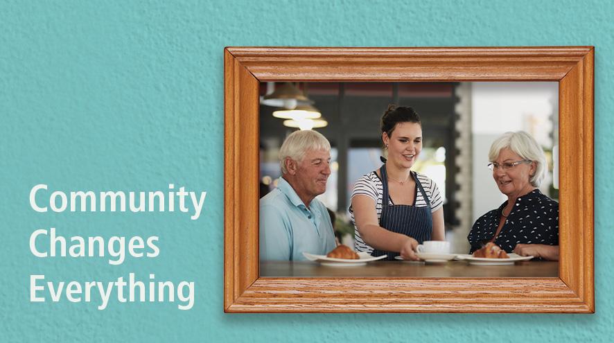Community Changes Everything text next to a framed picture of a man and a woman enjoying their server's company at a cafe..