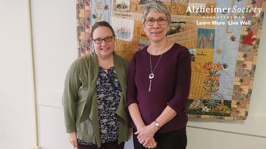 Our Dementia Community Coordinator standing in front of a patchwork quilt with Merle Willey