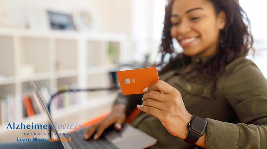 A woman smiling while holding a laptop and credit card 
