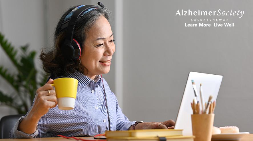 A woman sitting at her laptop with headphones on while enjoying a beverage in a yellow mug.