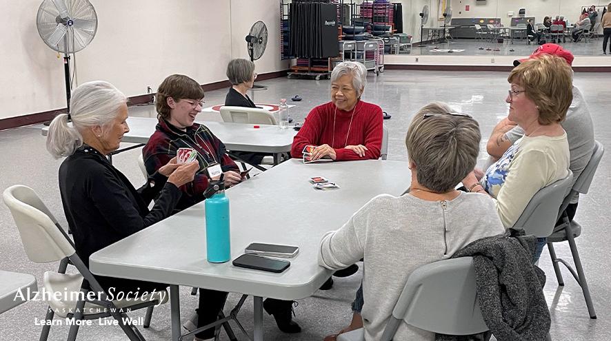 A group of people of mixed ages playing cards together and smiling.