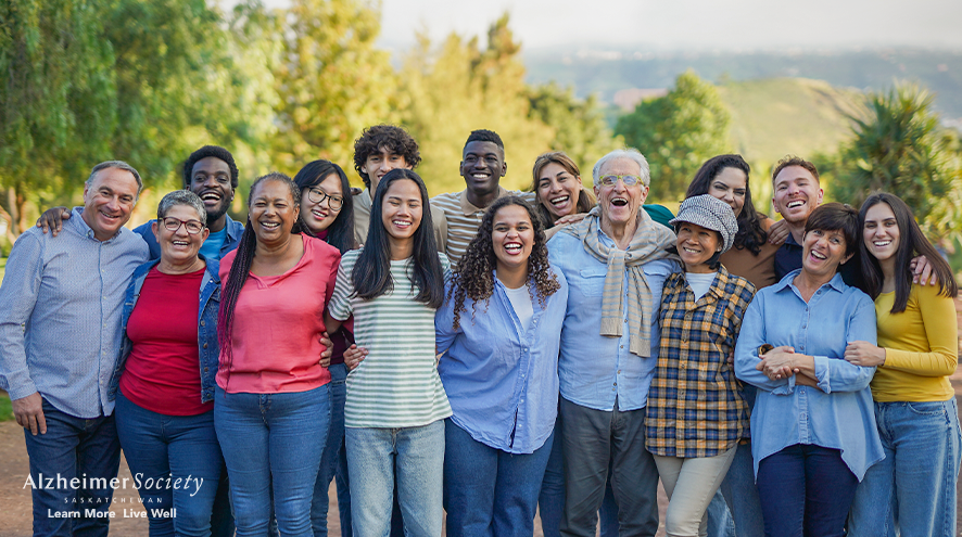 A group of 16 people of various ages and backgrounds standing in front of trees. You can see hills and a valley in the distance.