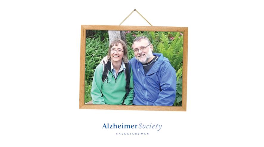 A picture frame with a photo of a woman and man sitting next to each other and smiling in a garden.