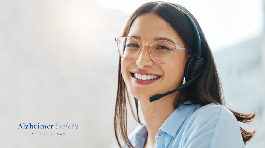 A woman in a blue collared shirt is wearing a headset and smiling. She is also wearing light coloured glasses.