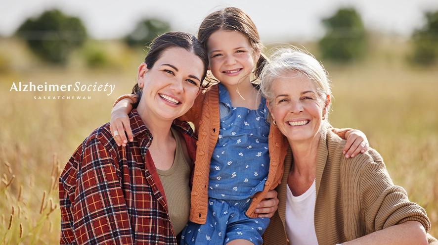 A woman with her adult daughter and young grandchild smiling with a field in the background.