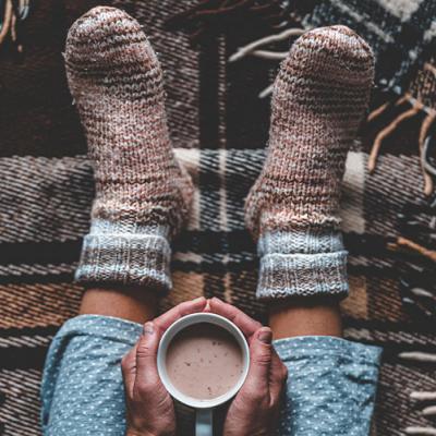 A picture of a person cozied up in a blanket with tea 