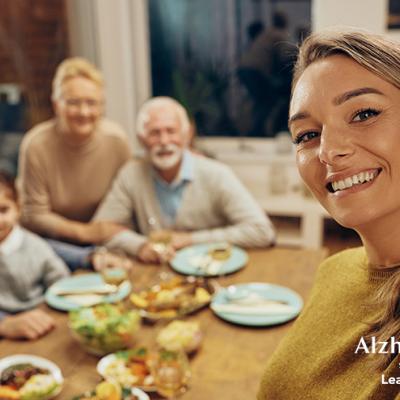 A woman taking a selfie in front of her extended family at the dinner table.