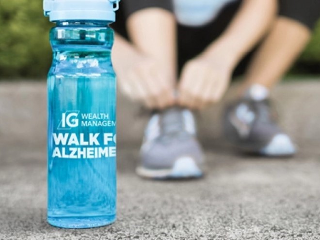 Water bottle branded with the IG Wealth Management Walk for Alzheimer's logo, with someone tying their shoelaces in the background.