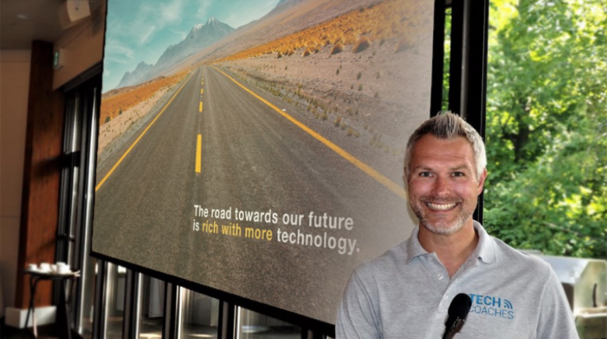 Image of Chris Bint, CEO and chief learning officer for Tech coaches, in front of a sign of the open road.