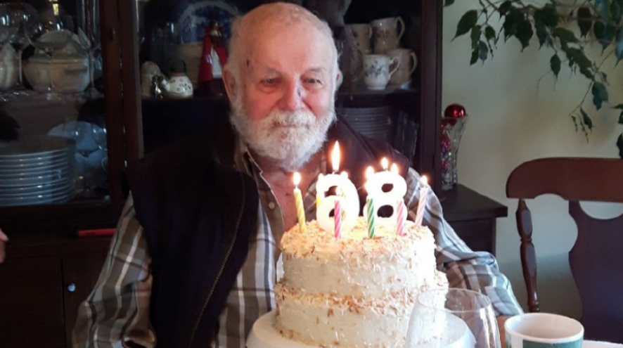 Bruce Howie sits in front of a two-tiered birthday cake with candles