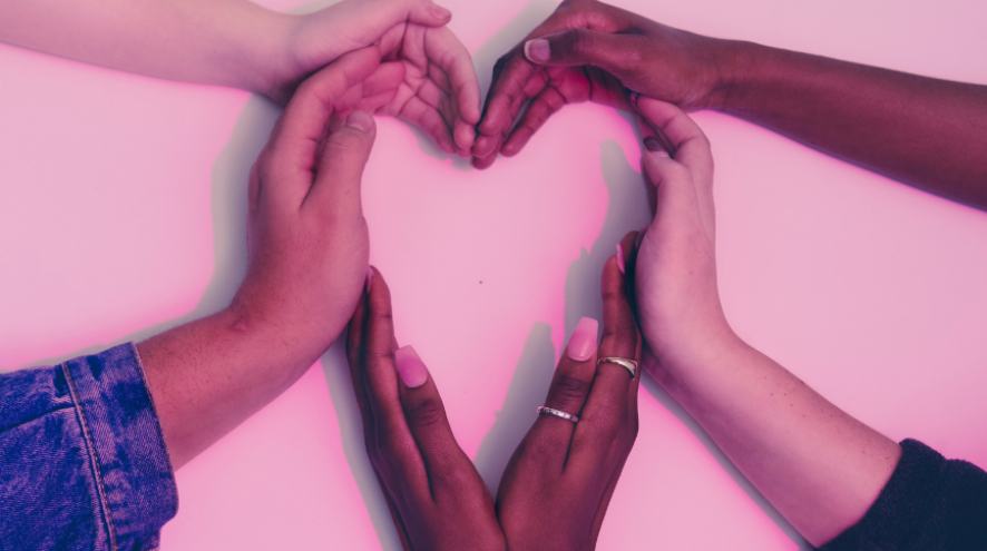 Pinkish picture of black and white hands making a heart.