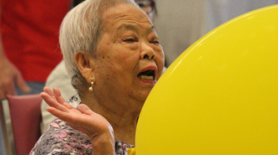 Head and shoulder shot of an older Asian woman hitting a big yellow ball
